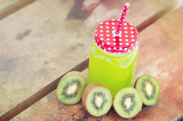 Green smoothie with kiwi in a glass with a red straw, wooden background