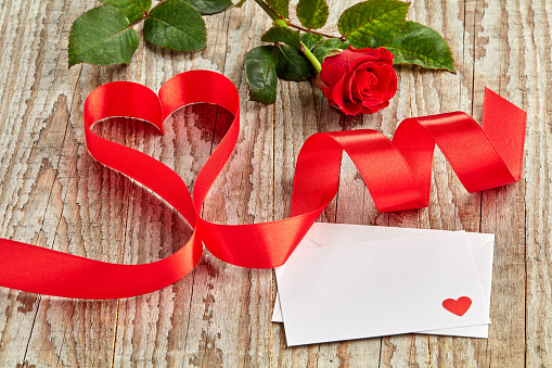 Red ribbon shaped into heart on wooden background with love letter