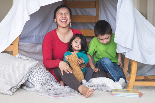Native American mom plays with her daughter and son under makeshift fort in living room