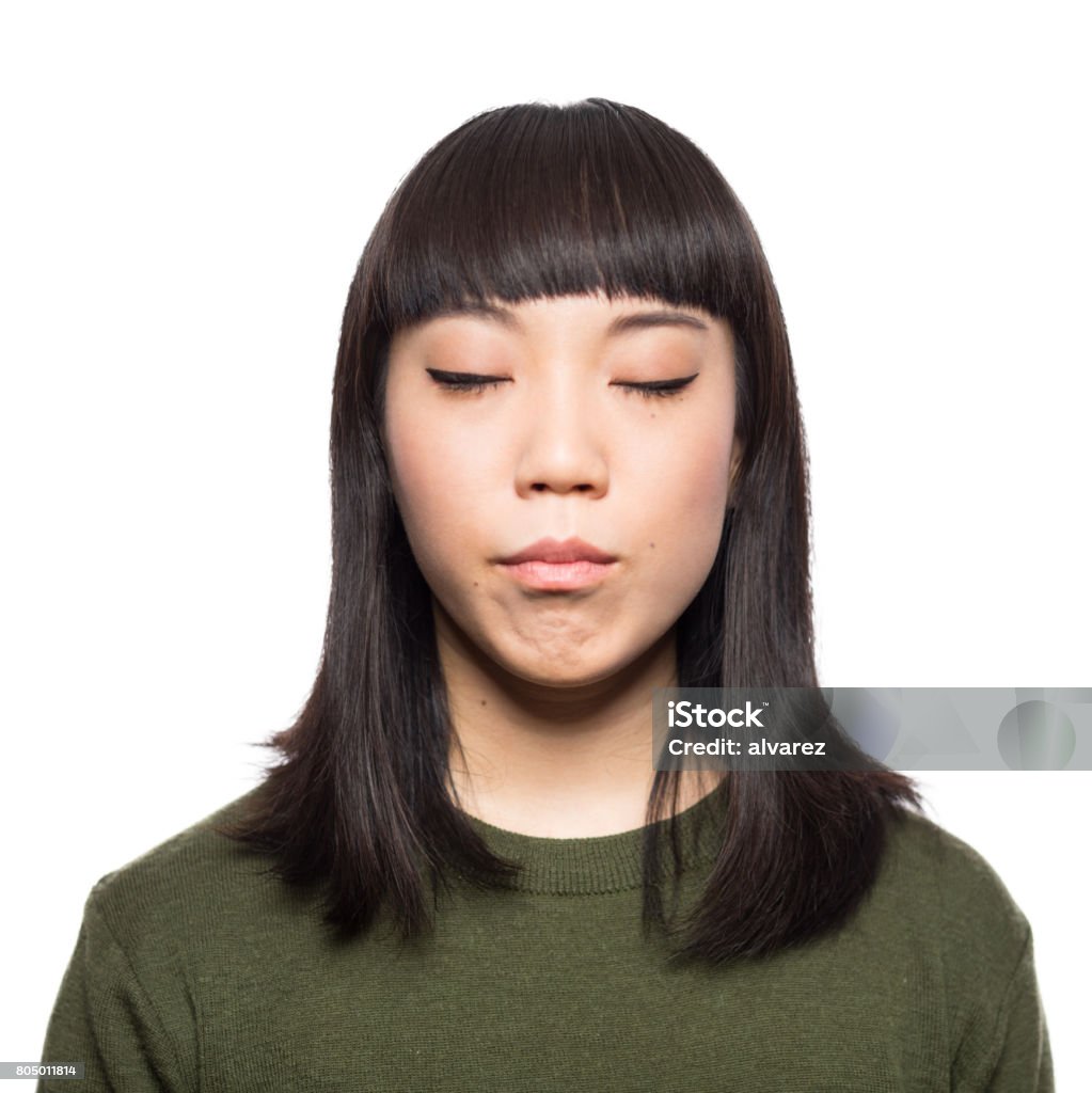 Portrait of young japanese woman with eyes closed Portrait of young japanese woman standing with her eyes closed against white background Eyes Closed Stock Photo