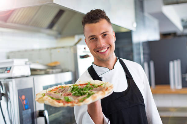 istock Smiling chef holding fresh pizza in kitchen 805020050