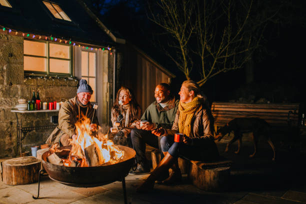 A Group OF Young Adults Roasting Marshmallows Around A Bonfire During Winter