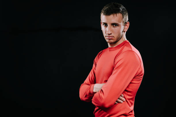 istock Attractive athlete man in red sportswear standing over dark background, thinking over problems in his life, holding hands and looking away. Lifestyle, sport, motivation. 805054278