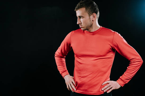 istock Handsome athlete man in red sportswear standing over dark background, thinking over problems in his life, holding hands on his waist, looking at one side. Lifestyle, sport, motivation. 805054326