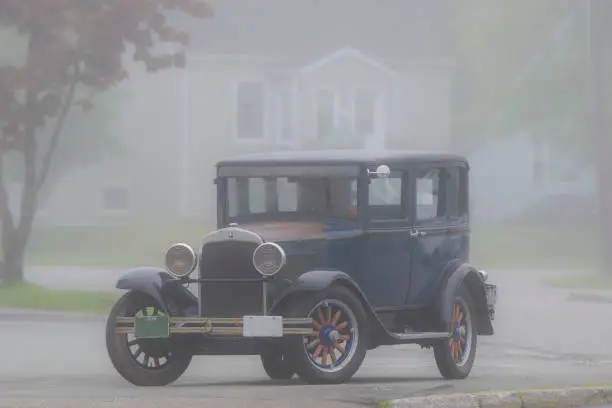 Antique car in fog. License plates blank except one has year 1928. 45 degree angle view from front. Car is parked. Room for text.