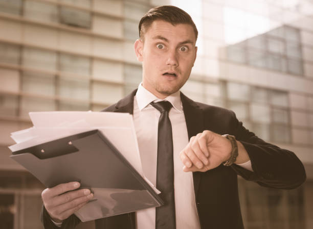 istock Man in suit is looking on watch near the office 805074514
