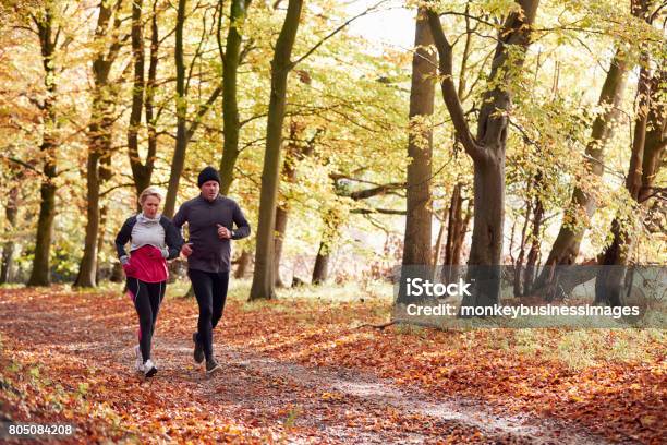 Mature Couple Running Through Autumn Woodland Together Stock Photo - Download Image Now