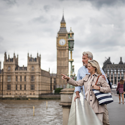 Woman pointing to man at Westminster Bridge. Mature couple is standing against Big Ben. They are in casuals.