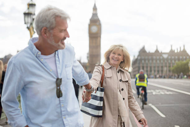 Smiling couple walking on Westminster Bridge Mature man pulling woman while walking on Westminster Bridge. Happy female is looking at male while holding hands against Big Ben. Couple is enjoying vacation at London. westminster bridge stock pictures, royalty-free photos & images