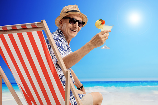 Mature man with a cocktail sitting in a deck chair on a beach