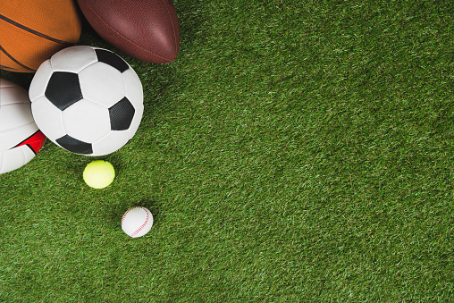top view of balls for soccer, basketball, tennis, baseball and american football on grass pitch