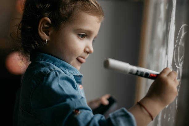 istock Cute kid with tongue out drawing on the window 805109408