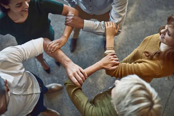 High angle shot of a group of colleagues linking arms in solidarity at work