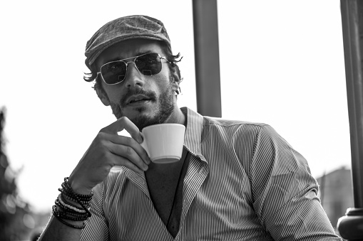 Black and white portrait of a young man drinking coffee while sitting in the cafe