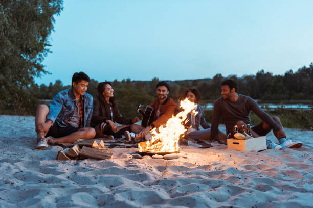 istock young multiethnic friends resting near campfire on sandy beach 805248154