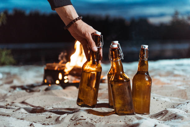 istock human hand taking bottle of beer from sand with campfire behind 805280732