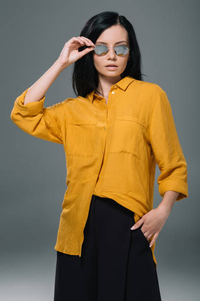 istock beautiful elegant model posing in yellow blouse and sunglasses, isolated on grey 805305254