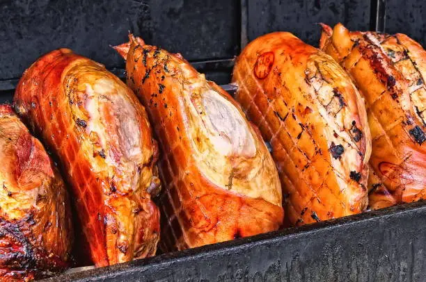 Photo of Pork ham meat is roasted on an open fire in the grill. Street Czech food. Prague, Czech Republic.