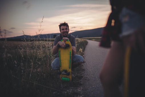 Hipster couple resting on the road while holding skateboards in their hands