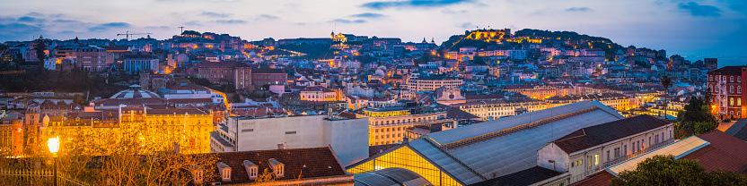 Panoramic view across the rooftops of Baixa to the hillside of Castelo Sao Jorge and the churches and villas of central Lisbon illuminated before dawn in the heart of Portugal’s vibrant capital city.