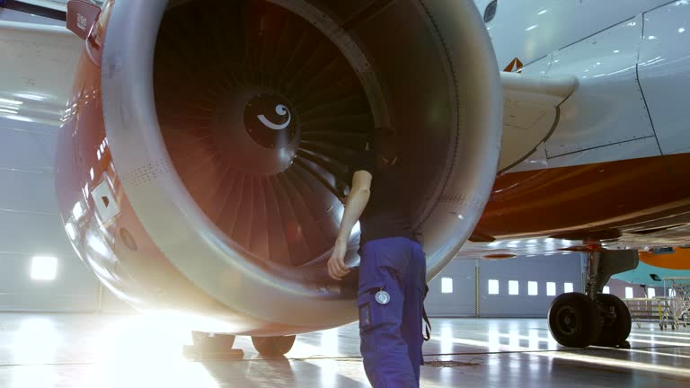 In a Hangar Aircraft Maintenance Engineer/ Technician/ Mechanic Inspects with a Flashlight Airplane's Jet Engine.