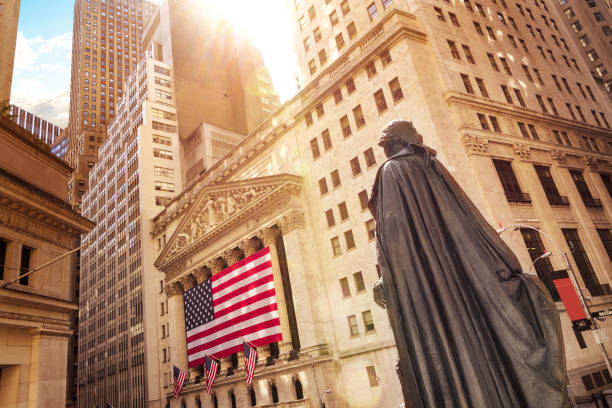 New York City, USA - September 7, 2023: Low angle view of American flag, office building exteriors, and Exchange’s Broad Street facade with classical portico, Corinthian columns, and pediment roof.