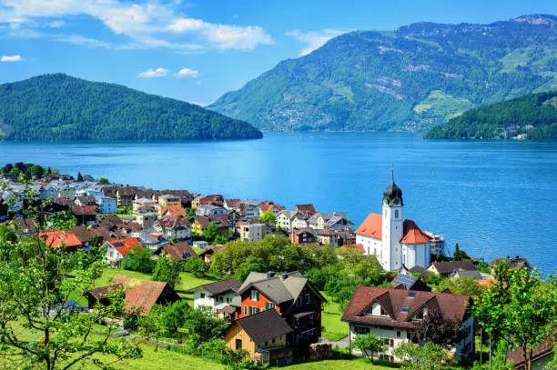 Little swiss town with white gothic church on the shore of Lake Lucerne, Alps mountains, Switzerland