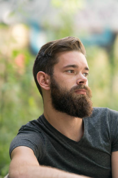 istock Handsome thoughtful bearded guy sitting on a bench in park 805628104