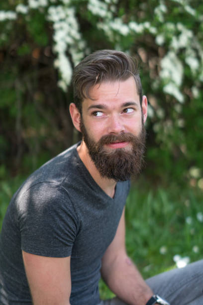 istock Young hipster with beard sitting with crossed legs in park 805651906