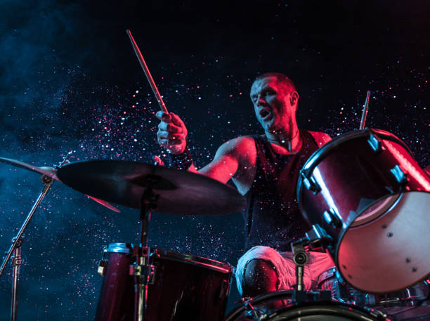 A man playing drums on stage with sparkles exploding off the drums.
