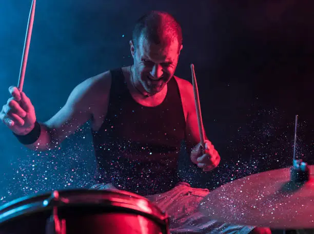 A man playing drums on stage with sparkles exploding off the drum.