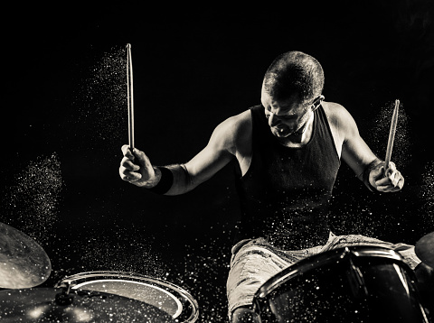 A black and white image of a man playing drums on stage with glitter sparkles exploding off the drums.