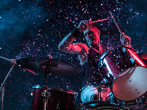 A man playing drums on stage with sparkles exploding off the drums.