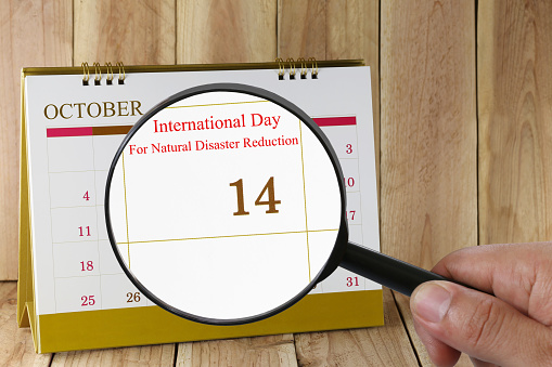 Magnifying glass in hand on calendar you can look International Day For Natural Disaster Reduction in 14 October,concept of a public relations campaign fight against natural disasters.