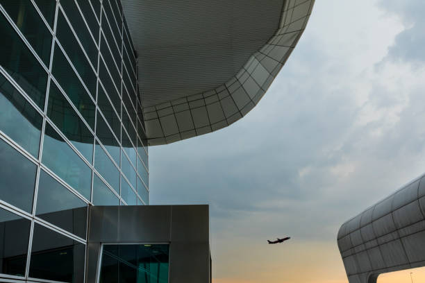 Modern architetural building with commercial airplane taking off At sunset time at Kuala Lumpur International Airport, commonly named KLIA, a commercial airplane take off in the horizon, with nice reflection on the glass modern architecture of the buildings. kuala lumpur airport stock pictures, royalty-free photos & images