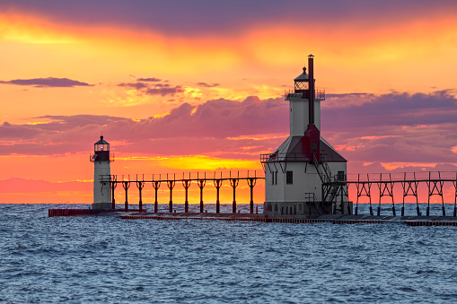 The St. Joseph, Michigan North Pier Inner and Outer Lighthouse shine their lights backed by a dramatic and colorful sunset on Lake Michigan.