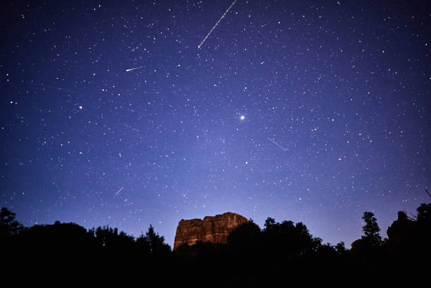 The famous Sedona red rocks rise against a night sky filled with shooting stars.