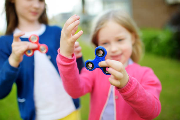 istock Two funny sisters playing with fidget spinners on the playground. Popular stress-relieving toy for school kids and adults. 805970118