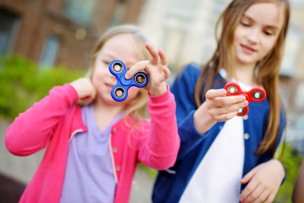 istock Two funny sisters playing with fidget spinners on the playground. Popular stress-relieving toy for school kids and adults. 805970246
