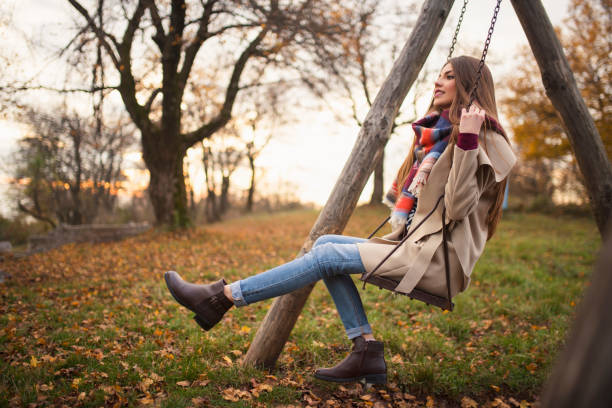 Beautiful young woman swinging in the park and enjoying a colorful autumn day.