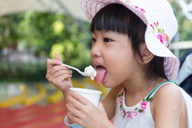 Asian Chinese little girl eating ice cream Asian Chinese little girl eating ice cream at outdoor park asian little chinese girls eating ice cream stock pictures, royalty-free photos & images