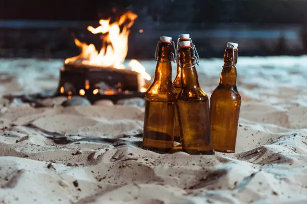 bottles of beer standing on sandy beach with bonfire behind