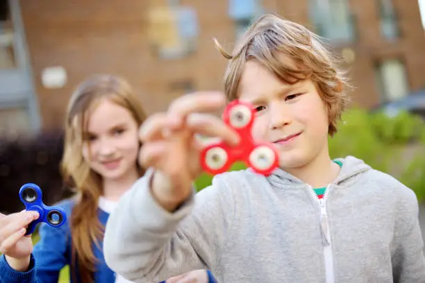 Photo of Two funny friends playing with fidget spinners on the playground. Popular stress-relieving toy for school kids and adults.