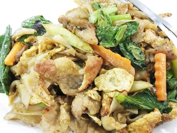 remuer les frites nouilles plates et porc à la pâte de haricots de soja conservé en blanc sur la table en bois. cuisine de style thaïlandais. - tofu chinese cuisine vegetarian food broccoli photos et images de collection