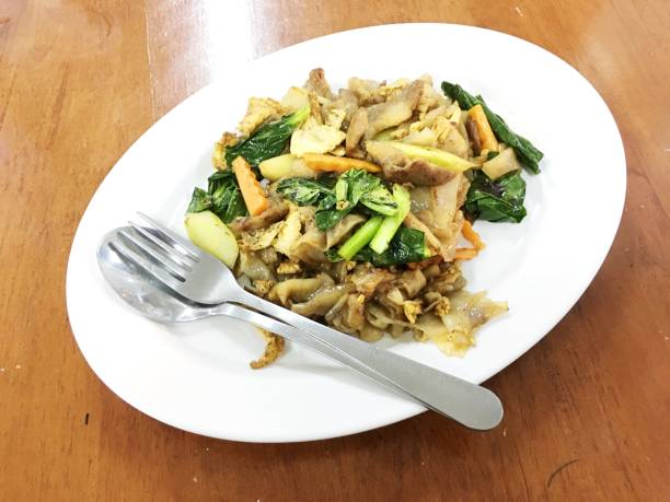 remuer les frites nouilles plates et porc à la pâte de haricots de soja conservé en blanc sur la table en bois. cuisine de style thaïlandais. - tofu chinese cuisine vegetarian food broccoli photos et images de collection