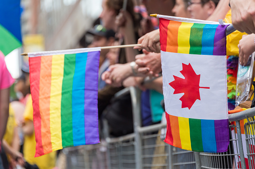 Toronto, Canada - 25 June 2017: Gay Pride Parade spectators holding canadian gay rainbow flags during Toronto Pride Parade in 2017