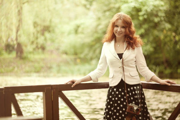 Longhair redhead girl wearing a grey coat standing on the edge of the hill in front of the forest of the mountain. Concept (idea) of freedom, dreaming, thinking, meditation, and motivation. Cloudy spring afternoon.