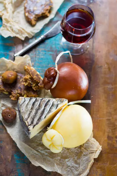 Sweet dessert liqueur wine in glass, hard cheeses Caciocavallo or Provolone, Tomme de Montagne, dried figs with figs bread, still life on wooden platter