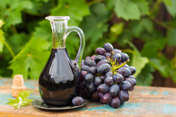 negro viejo vinagre balsámico en una jarra de cristal con uvas rojas sobre fondo verde viña - balsamic vinegar bottle vinegar red wine fotografías e imágenes de stock