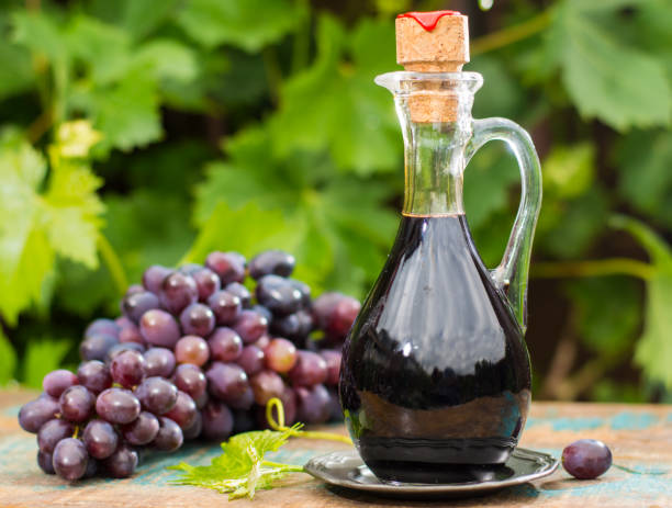 Black old balsamic vinegar in a glass jug with fresh red grapes on green vineyard background Black old balsamic vinegar in a glass jug with fresh red grapes on green vineyard background on wooden table, outside balsamic vinegar stock pictures, royalty-free photos & images